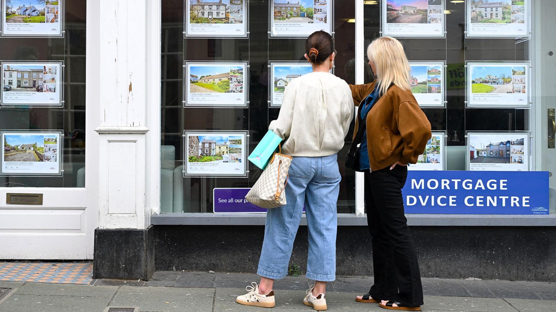 Two women looking at an estate agent window in Cardigan, Wales. Photo: Getty Images, via BBC News.
